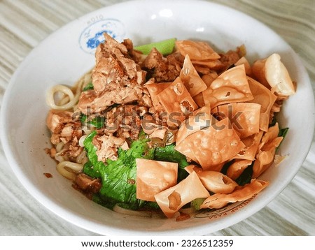 close up of chicken noodles topped with greens, soy sauce chicken and fried dumplings in a white bowl. Indonesian people's favorite food at economical prices