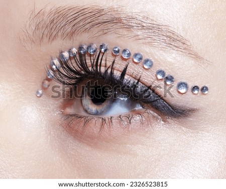 Closeup macro shot of human female eye with unusual makeup. Woman with rhinestones arrows on eyelid. Royalty-Free Stock Photo #2326523815