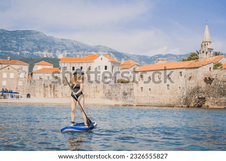 Young women Having Fun Stand Up Paddling in blue water sea in Montenegro. Against the backdrop of the Old Town of Budva. SUP