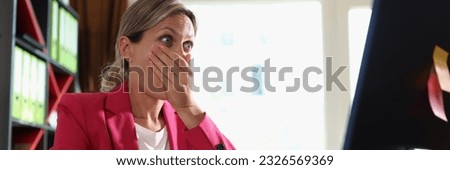 Portrait of surprised woman sitting at workplace and looking at computer display. Shocked woman covering mouth with hand. Face expressions concept