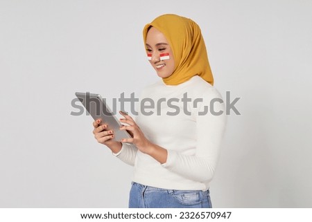 Smiling young Asian Muslim woman wearing a hijab using digital tablet isolated over white background. Celebrate Indonesian independence day on 17 August