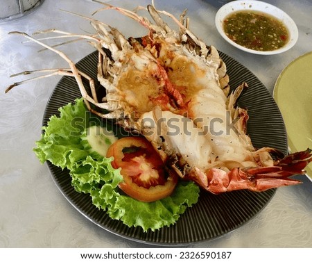 The picture of the grilled river prawn was cut in the middle of the body to see the orange shrimp on the head. White meat is placed on a plate and served with spicy seafood dipping sauce.