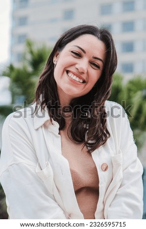 Vertical individual portrait of young adult woman smiling and looking at camera with white tooth standing outdoors. Front view of happy teenage girl with positive expression. Cheerful lady laughing