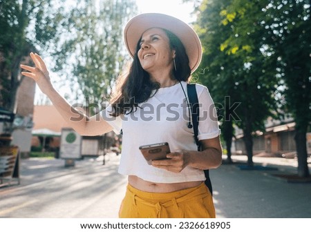 Traveler girl is looking for a way in an unfamiliar city using phone and maps. Tourism, visiting new places, communication with passers-by. Modern technologies, digitalization, mobile phone navigation