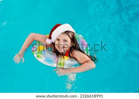 a happy blonde girl in a Santa Claus hat and a lifebuoy is swimming in the pool