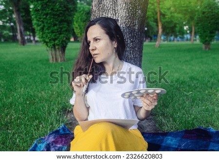 Art therapy. Woman draws in the park. Girl sits with her back against a tree and looks into distance. Restoration of nervous system with help of drawing. Concept of relaxation and meditative state