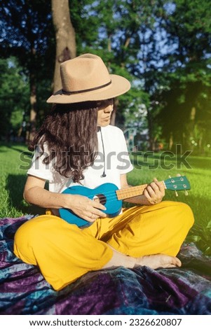 Girl in the park sitting on the grass plays the ukulele. Learning to play a four-string instrument. Relaxation in a public park. Music therapy, psychology, meditation, relaxation, relaxation