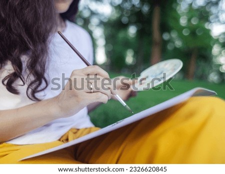 Art therapy. Woman draws in the park. Girl sits with her back against a tree and looks into distance. Restoration of nervous system with help of drawing. Concept of relaxation and meditative state