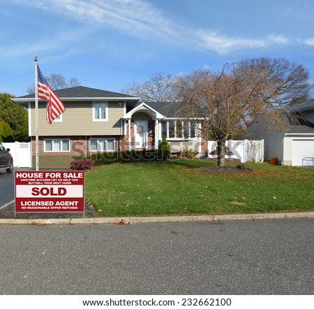 American Flag pole Real Estate sold (another success let us help you buy sell your next home) sign suburban high ranch home autumn day residential neighborhood blue sky clouds USA