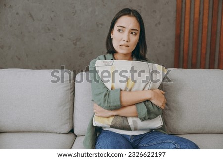 Young sad frustrated upset woman of Asian ethnicity wears casual clothes hugging holding pillow sits on grey sofa couch stay at home hotel flat rest relax spend free spare time in living room indoor Royalty-Free Stock Photo #2326622197