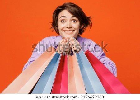 Young happy cool excited woman wearing purple shirt casual clothes hold in hand paper package bags after shopping isolated on plain orange color background studio. Black Friday sale buy day concept