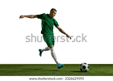 Young man in green uniform, football in motion, playing, kicking ball on sports field against white background. Concept of professional sport, action, lifestyle, competition, hobby, training, ad Royalty-Free Stock Photo #2326629595