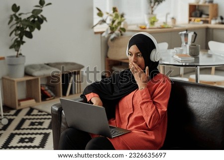 Young terrified or surprised, Muslim woman covering mouth with hand while looking at laptop screen and watching thriller or terrifying video Royalty-Free Stock Photo #2326635697