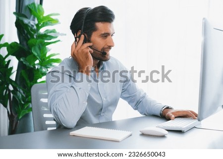Male call center operator or telesales representative siting at his office desk wearing headset and engaged in conversation with client providing customer service support or making a sale. fervent Royalty-Free Stock Photo #2326650043