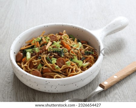 Fried Noodles or Mie Goreng or bakmi goreng is a traditional Indonesian stir fried noodle dish mixed with vegetables and sausage. served on white pan. selected focus 