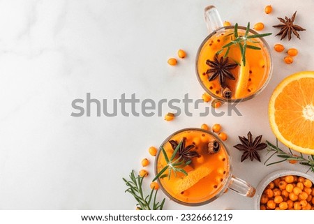 Cups of sea buckthorn tea with orange, berries, cinnamon and rosemary on white table. Healthy herbal autumn drink Royalty-Free Stock Photo #2326661219