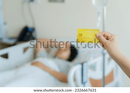 Show credit card in hand while Asian female patient lying on the bed. Woman patient prepares to pay medical expenses. Female patient with credit or health card for medical treatment. Health Insurance. Royalty-Free Stock Photo #2326667631