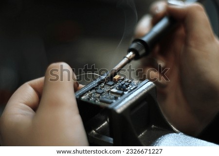 A female electronics technician is shown in close-up in a professional workshop while working with tin soldering parts. She repairs electronic devices and handles electrical equipment. She is solderin Royalty-Free Stock Photo #2326671227