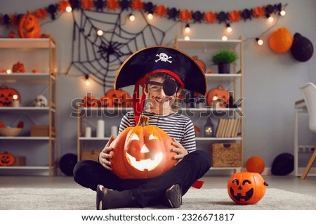 Portrait of smiling little boy child in costume sit pose with jack-o pumpkin with candle celebrate Halloween. Happy small kid dressed as pirate enjoy fall scary celebration. All saints eve.