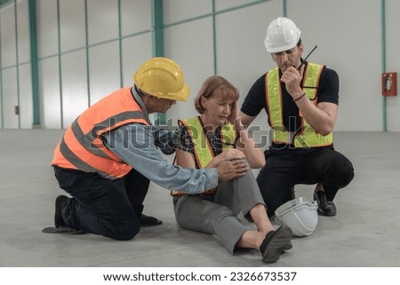 Factory engineer helping injured employee Notification of incidents to the medical team in the warehouse of a large industrial factory.Multiethnic teamwork and Wearing safety devices at work concepts.