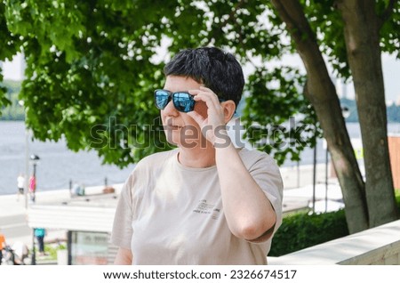 Portrait of middle-aged woman with black short hair and sunglasses. A woman looks into the distance, standing against the backdrop of trees on a sunny summer day