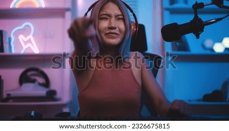 Portrait Young Asian woman professional gamer wearing headphone to gaming on pc and talking with team on microphone with fun while competition, cast gameplay or record a podcast in neon light room