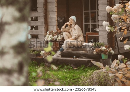 woman gardener relaxing in cozy autumn day, sitting on wooden stairs at house entryway. Enjoying warm october in the countryside, spending weekend outdoor Royalty-Free Stock Photo #2326678343