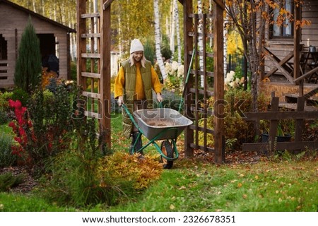 seasonal autumn garden work. Woman gardener at wooden pergola with wheelbarrow. Natural country living Royalty-Free Stock Photo #2326678351