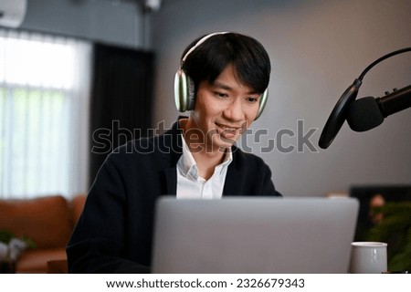 Young man recording a podcast on his laptop computer with headphones and a microphone. Male podcaster making audio podcast from his home studio.