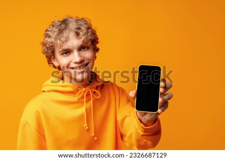 Young smiling man holding smartphone with blank device screen against yellow background