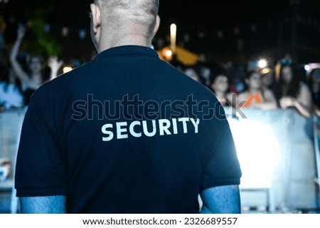 The security guard wears a T-shirt with the inscription security. A security guard stands in front of the audience during a music festival.