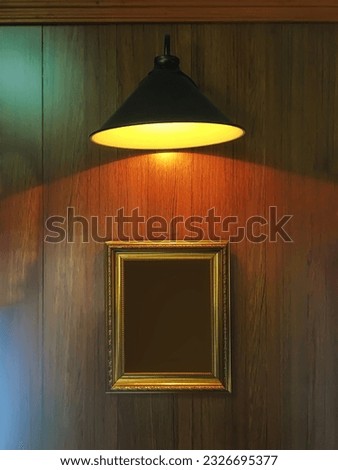 A wooden wall with picture frames under a yellow lamp.