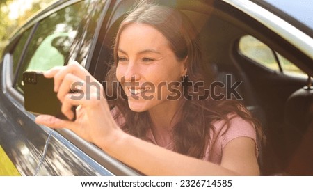 Woman In Car On Road Trip Vacation Taking Picture On Mobile Phone