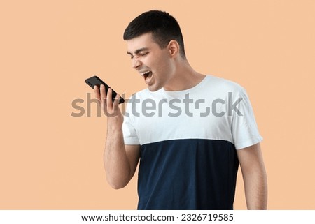 Stressed young man with smartphone on beige background