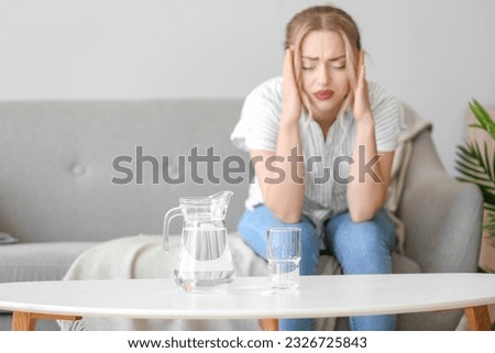 Jug and glass of water with soluble tablet on table in room, closeup