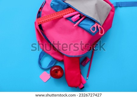 Pink school backpack with apple, ruler and markers on blue background