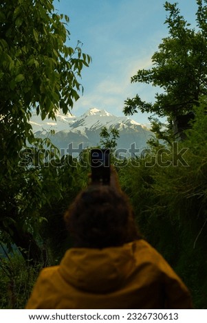 A woman taking picture of snow-capped mountains during sunset.