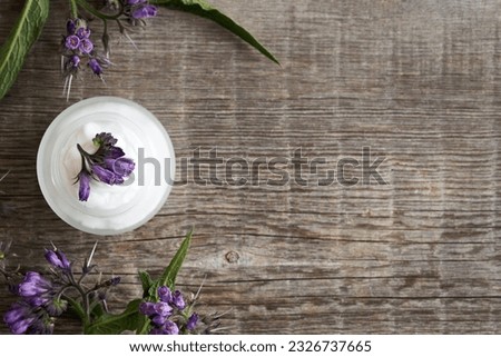 A jar of comfrey ointment with fresh blooming Symphytum plant on wooden background with copy space