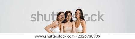 Three young positive smiling attractive ladies pose and hold poster standing in studio isolated over white background Royalty-Free Stock Photo #2326738909
