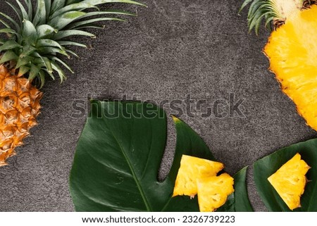 Top view of fresh cut pineapple with tropical leaves on dark gray table background.