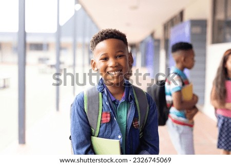Portrait of smiling african american schoolboy in elementary school corridor, with copy space. Education, inclusivity, elementary school and learning concept. Royalty-Free Stock Photo #2326745069
