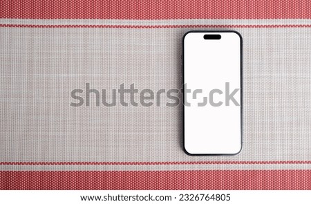 The smartphone is placed on the red and cream colored cloth.