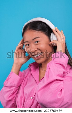 smiling asian girl looking at the camera while listening to music with wireless headphones