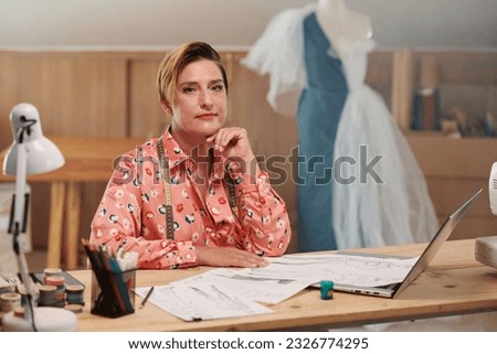 Portrait of mature woman sitting at desk and working with fashion sketches