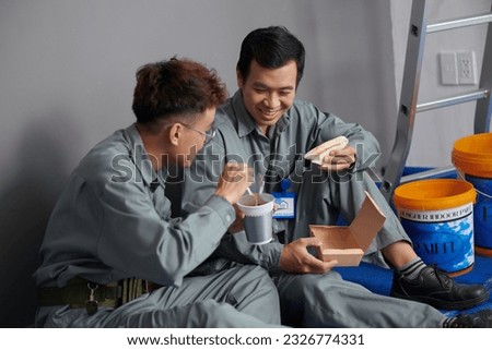Builders eating instant noodles and sandwiches for lunch at construction site Royalty-Free Stock Photo #2326774331