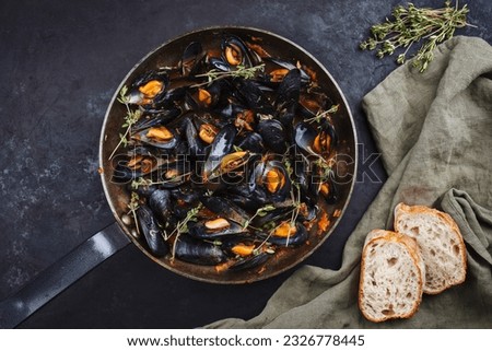 Traditional barbecue Italian blue mussel in tomato red wine sauce with baguette bread as top view in a rustic iron pan  Royalty-Free Stock Photo #2326778445