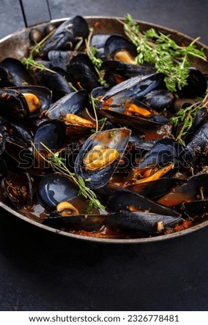 Traditional barbecue Italian blue mussel in tomato red wine sauce with herb and garlic as close-up in a rustic iron pan  Royalty-Free Stock Photo #2326778481