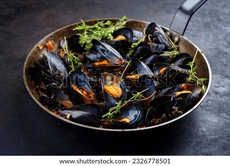Traditional barbecue Italian blue mussel in tomato red wine sauce with herb and garlic as close-up in a rustic iron pan  Royalty-Free Stock Photo #2326778501