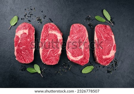 Four raw dry aged wagyu rib-eye beef steaks with herb and black salt offered as top view on a black board with copy space Royalty-Free Stock Photo #2326778507