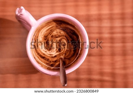 Instant coffee with milk in a pink mug on a wooden table, top view, sunny weather